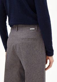 Grau gemusterte Hose mit geradem Schnitt, ausgestattet mit einer einzigen Gesäßtasche und einem Etikett auf dem Bund. Hochwertige Stofftextur.