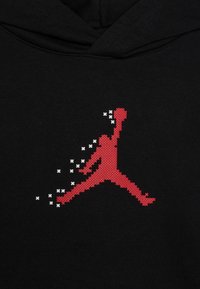 Silhouette pixelata rossa di un giocatore di basket che salta con un braccio sollevato e tiene una palla su uno sfondo di tessuto nero.