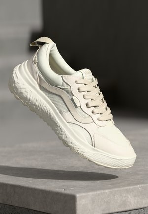 Cream-colored Vans sneakers with a textured mesh upper, smooth leather accents, lace-up front, and a thick, patterned rubber sole.