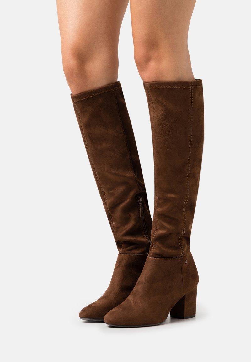 Botas marrones de ante por encima de la rodilla con punta redondeada y tacón cuadrado. Incluyen una cremallera lateral y un detalle de costura vertical.