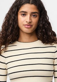 Ζακέτα από ριμπ μώβ σε κρεμ απόχρωση με μαύρες οριζόντιες ρίγες, διαθέτοντας στρογγυλή λαιμόκοψη και εφαρμοστή σιλουέτα.