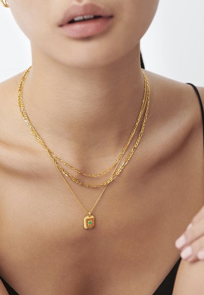 Suurendatud pilt inimesest, kes kannab kolme kihilist kuldkaelakeed, üks neist on ristküliku kujuga ripats, millel on väike roheline kalliskivi.