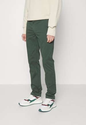 Groene katoen chinos met een slim fit, aangevuld met een lichtbeige sweatshirt en witte sneakers met groene en bordeauxrode accenten.