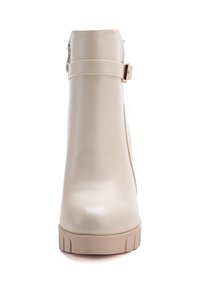 Botines beige de material sintético, con textura suave, punta redonda y cremallera lateral con una correa decorativa y hebilla.