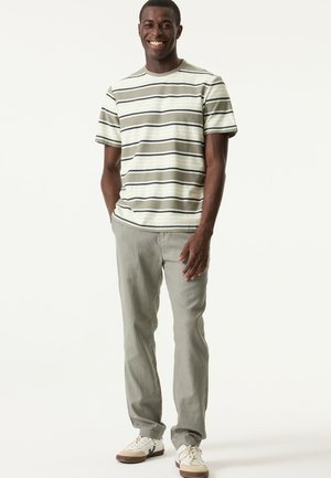 Maglietta a righe verde chiaro con maniche corte, abbinata a pantaloni grigio chiaro e sneakers bianche con dettagli marroni.