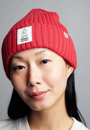 Punainen neulepipo, jossa on ribbikuvio, huippupiste ja valkoinen logo. Hattu istuu tiukasti päähän.