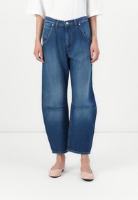 Denim jeans with a blue wash, wide-leg design, visible stitching, and knee patches. Styled with a white top and pink flats.