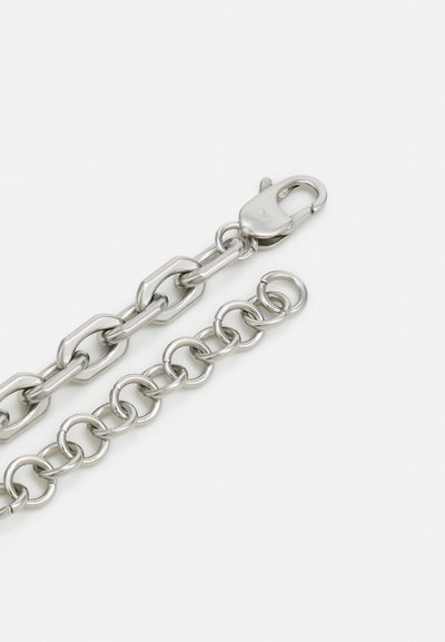 Corrente de metal prateado com elos ovais e redondos alternados, encerrando-se com um fecho de mola. Textura suave e acabamento polido.