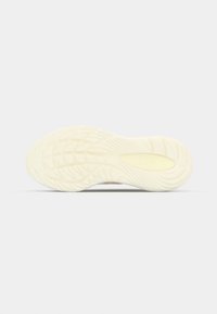 Semelle d'une sneaker crème montrant un motif de bande de roulement ondulé et rainuré avec un logo ovale près du talon.