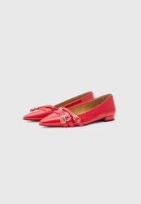 Ballerines fermées rouge vif avec des bouts pointus et des straps décoratifs dotés de boucles. Finition brillante et petit talon pour un confort optimal.