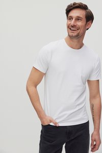 Witte katoenen t-shirt met een ronde hals en korte mouwen, gecombineerd met donkere spijkerbroeken. Glad textuur, aansluitend ontwerp en minimale details.