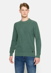 Pulover verde tricotat, cu guler rotund, mansete și tiv cu nervuri. Are un model texturat, etichetă pe partea inferioară și o croială lejeră.
