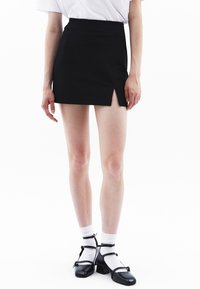 Zwarte mini rok met een splits aan de voorkant, gecombineerd met witte sokken en zwarte Mary Jane schoenen. Geschikt voor een gladde stof en een op maat gemaakte pasvorm.