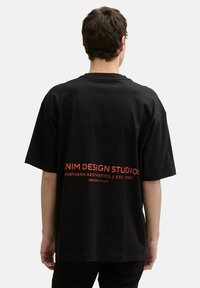 Black oversized T-shirt made of cotton with short sleeves. Features graphic text in red on the back, stating "DENIM DESIGN STUDIO."