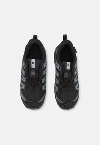 Chaussures de sport noires avec une tige texturée, des accents gris et un système de laçage rapide. La semelle est conçue pour une bonne traction.