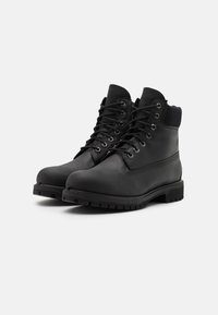 Bottines en cuir waterproof noir, à lacets sur le devant, avec une semelle en caoutchouc robuste, un col rembourré et un logo proéminent sur le côté.