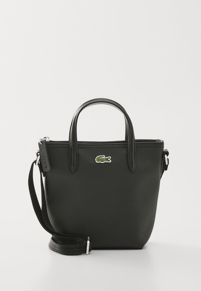 Sac fourre-tout synthétique noir avec doubles poignées, bandoulière amovible, fermeture éclair et accent du logo crocodile vert de Lacoste.