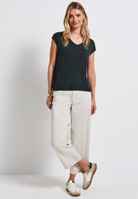 Tmavě zelený krátký rukáv V-krk top, uvolněný střih, spárovaný se světle béžovými širokými kalhotami a béžovými teniskami s texturovanou podrážkou.