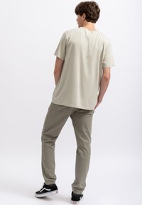 Lichtgrijs t-shirt met korte mouwen, zachte stof, relaxte pasvorm. Gecombineerd met olijfgroene broeken en zwarte sneakers met witte accenten.
