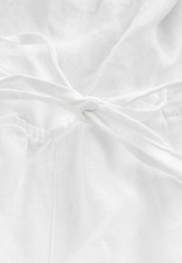 Gros plan sur un tissu blanc avec un nœud de cordon noué et des coutures visibles sur une surface textile texturée.