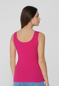 Top ajustado sin mangas en un brillante color rosa. Tela suave y elástica con un diseño de escote en la espalda. Combinado con jeans de denim de cintura alta.