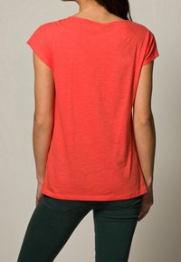 Relaksujący koralowy t-shirt z krótkim rękawem, okrągłym dekoltem i nieco dłuższym tyłem. Miękka tkanina o gładkiej fakturze, prosty design.