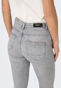 Γκρι τζιν παντελόνι από ντένιμ με μεσαίο καβάλο, πίσω τσέπες και μαύρη ετικέτα με χρυσά γράμματα. Το ύφασμα έχει μια λεπτή υφή και κλασική εφαρμογή.