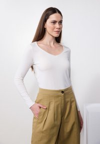 Long-sleeve white top with a V-neck design, paired with high-waisted, pleated khaki pants featuring side pockets and a button closure.