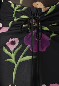 Gonna a fiori con tessuto in rete nera, caratterizzata da fiori vivaci in rosa e viola, con dettaglio arricciato in vita e nastri regolabili.