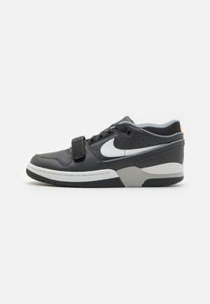 Baskets basses noires et grises avec une semelle blanche, un logo Nike blanc, des lacets et une bride noire à l'avant.