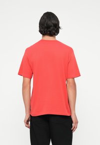 Tricou scurt cu mânecă roșie, cu guler rotund și o potrivire lejeră, fabricat dintr-un material moale de bumbac. Design simplu, fără modele sau accente vizibile.