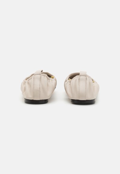 Ballerine in pelle beige con forma arrotondata, colletto elasticizzato e piccolo tacco nero. Presentano dettagli decorativi in tonalità oro sui lati.