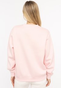 Helles rosa Sweatshirt mit Rundhalsausschnitt und überschnittenen Schultern, mit gerippten Bündchen und Saum, aus weichem Material mit glatter Textur.
