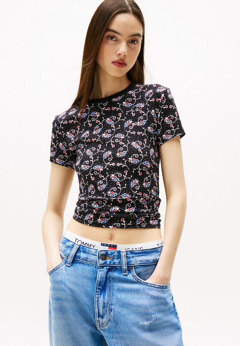 Czarny t-shirt w kwiaty z krótkim rękawem, z wielokolorowymi wzorami florystycznymi i dopasowanym krojem, w zestawieniu z jasnoniebieskimi dżinsami.