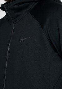 Chaqueta negra con cremallera de Nike, confeccionada en tejido texturizado, con un cuello alto, paneles laterales y un sutil logotipo negro en el pecho.