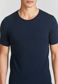 Maglietta a maniche corte blu navy in una morbida miscela di cotone. Presenta un colletto rotondo e un design aderente con una texture liscia.