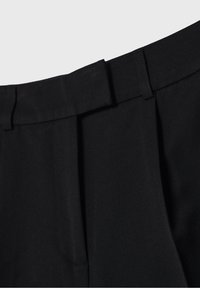 Pantalones negros de corte entallado con frente plano, que presentan pliegues sutiles, una textura suave y una cinturilla estructurada para un aspecto pulido.