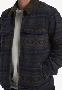 Navy and brown patterned flannel jacket with a faux fur collar, featuring two chest pockets and a zip front. Soft texture and tribal design.