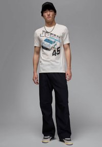 Camiseta gráfica blanca con un diseño de coche y el texto "JORDAN 45". Combinada con pantalones holgados negros y zapatillas grises con detalles en negro.
