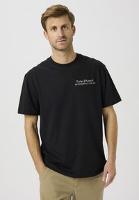 Fekete pamut rövid ujjú póló fehér felirattal, amelyen a "Porte d'Auteuil" és koordináták szerepelnek az elején. Klasszikus kerek nyakú kialakítás.