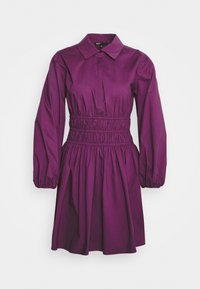 Robe violette avec col, manches longues bouffantes et taille élastiquée. En tissu lisse, elle présente une jupe froncée.