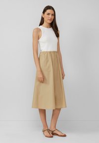 Tan midi skirt with elastic waistband, paired with a white sleeveless top. Model wears flat sandals. Simple and clean design with pockets.