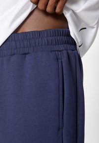 Merenmatskblå sweatpants med elastisk midjeband och sidofickor, med en slät yta och avslappnad passform. Synlig ljusgrå tröja under.