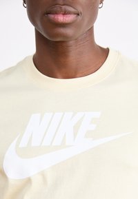 Camiseta de algodón amarillo claro con un gran logo blanco de Nike. El cuello es redondo y la tela parece suave con un corte relajado.