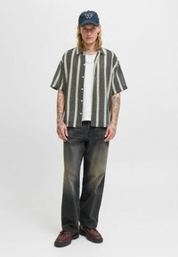Camisa de manga corta a rayas verticales en blanco y negro, combinada con jeans grises y zapatos gruesos marrones. Además, se lleva una gorra negra.