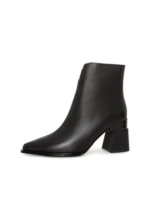 Botte de cheville noire avec un bout pointu et un talon bloc, présentant une finition en cuir lisse et une fermeture éclair élégante sur le côté.