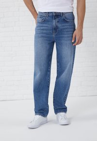 Lichtblauwe denim jeans met een recht gesneden ontwerp, vervaagde voorkant, vijf-pocket stijl en een knoop- en ritssluiting. Gecombineerd met witte sneakers.