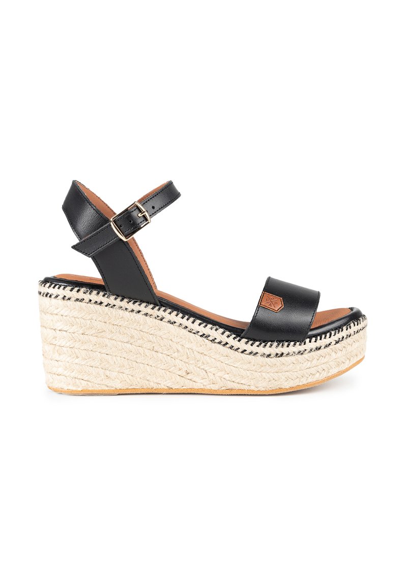 Sandalias de cuña de cuero negro con suela de yute. Presentan una correa en el tobillo con hebilla y una plantilla suave y plana. Costuras decorativas en la suela.