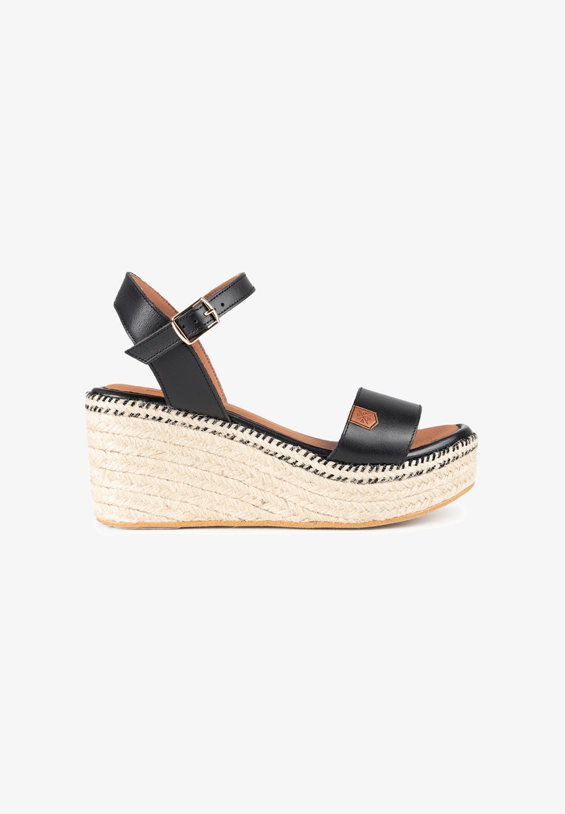 Sandalias de cuña de cuero negro con suela de yute. Presentan una correa en el tobillo con hebilla y una plantilla suave y plana. Costuras decorativas en la suela.