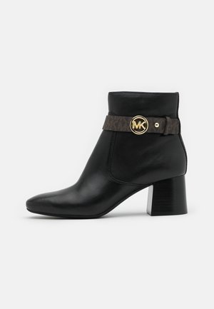 Bottine en cuir noire avec talon bloc, bride marron et boucle dorée avec logo MK sur le côté.